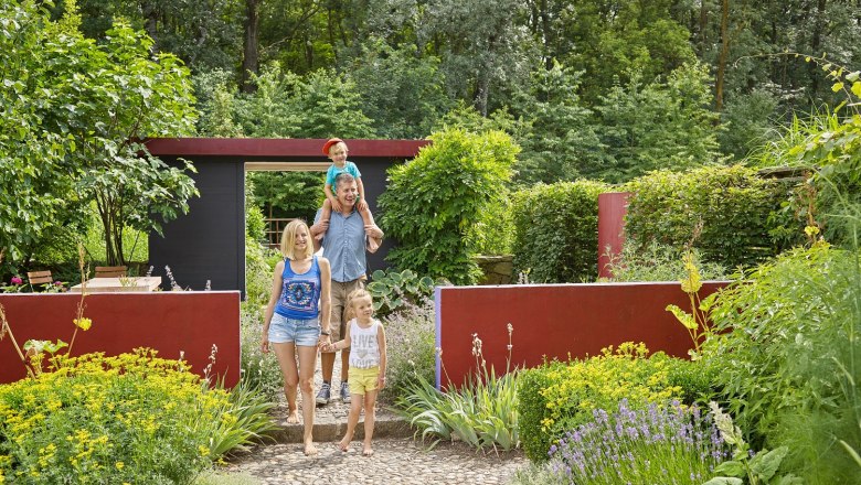 Familienerlebnis, © DIE GARTEN TULLN Familie spaziert durch einen Garten mit bunten Blumen und grünen Büschen.