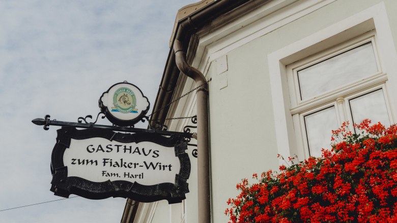 Wirtshaus in Langenlois, © Niederösterreich Werbung/Rita Newman Schild des Gasthauses zum Fiaker-Wirt in Langenlois mit roten Blumen am Fenster.