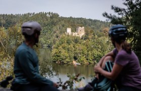 Kamptal Radweg, © Waldviertel Tourismus, Erwin Haiden Die sanften Hügel des Kamptals umarmen die malerische Ruine Dobra, die majestätisch über dem glitzernden Wasser thront. Radfahrer genießen hier eine wohlverdiente Pause, während sie den atemberaubenden Blick auf die umgebende Natur und die historische Architektur bewundern. Ein Ort, der zum Verweilen und Träumen einlädt.