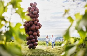 WEINWEG Langenlois, © Waldviertel Tourismus, Gerhard Wasserbauer Zwei Personen spazieren an einer großen Skulptur aus kugelförmigen Elementen vorbei, umgeben von Weinbergen.