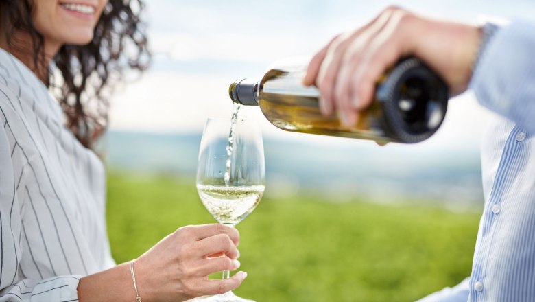 Ursin Haus, © © Waldviertel Tourismus, Gerhard Wasserbauer Eine Person schenkt Weißwein in ein Glas, das von einer anderen Person gehalten wird, im Hintergrund ein Weinberg.