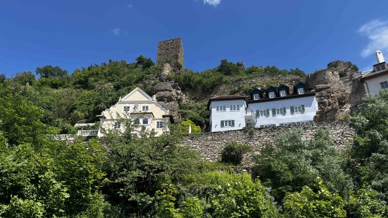 Blick auf Dürnstein, © Trailfex Blick auf Dürnstein mit historischen Gebäuden und Ruinen auf einem Hügel, umgeben von grüner Vegetation und blauem Himmel.