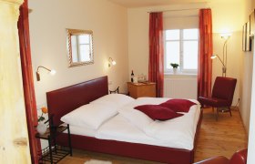 Genießerzimmer Cobaneshof, © Cobaneshof Gemütliches Schlafzimmer mit rotem Bett und Dekor.