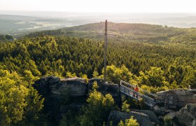 Nebelstein Ausblick, Landschaft, Kreuz, Thayatalweg 630, Zusatzetappe Weg entlang der Lainsitz, © Waldviertel Tourismus, Melanie Többe Aussichtsplattform auf einer Felsformation mit Blick über dicht bewaldete Hügel im Waldviertel, unter einem klaren blauen Himmel.