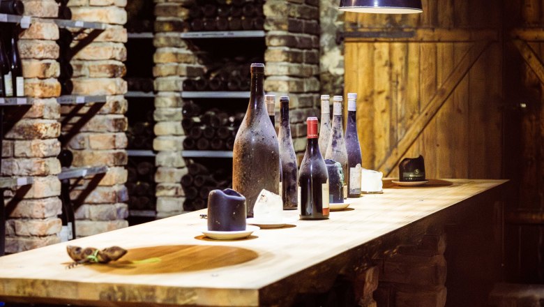 Steininger LOISIUM WeinWelt, © Pamela Schmatz Ein Weinkeller mit Ziegelwänden, Regalen voller Weinflaschen und einem Holztisch mit mehreren Weinflaschen darauf.