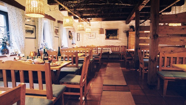 Heuriger Rebstockgrill Höfinger, © Weingut Höfinger Gemütlicher Innenraum eines traditionellen Heurigen mit Holzmöbeln und gedeckten Tischen.