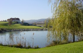Golfclub Lengenfeld, © Golfclub Lengenfeld Landschaft mit Golfplatz, Teich und Gebäude im Hintergrund.