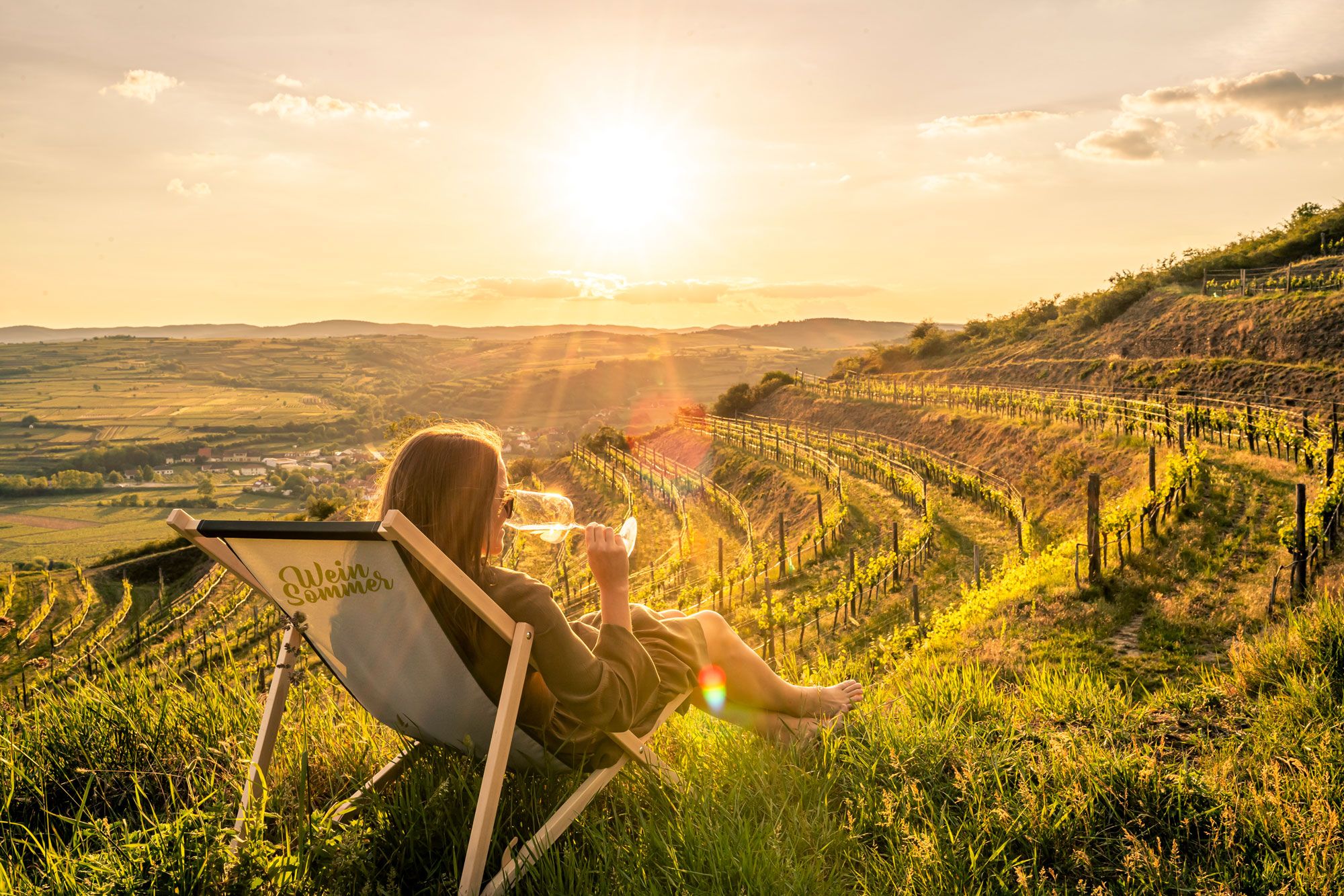 Eine Frau in einem Liegestuhl. Im Hintergrund die Weinberge.