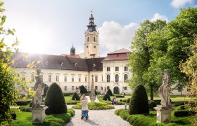 Barockes Stift mit Garten und Statuen im Vordergrund.