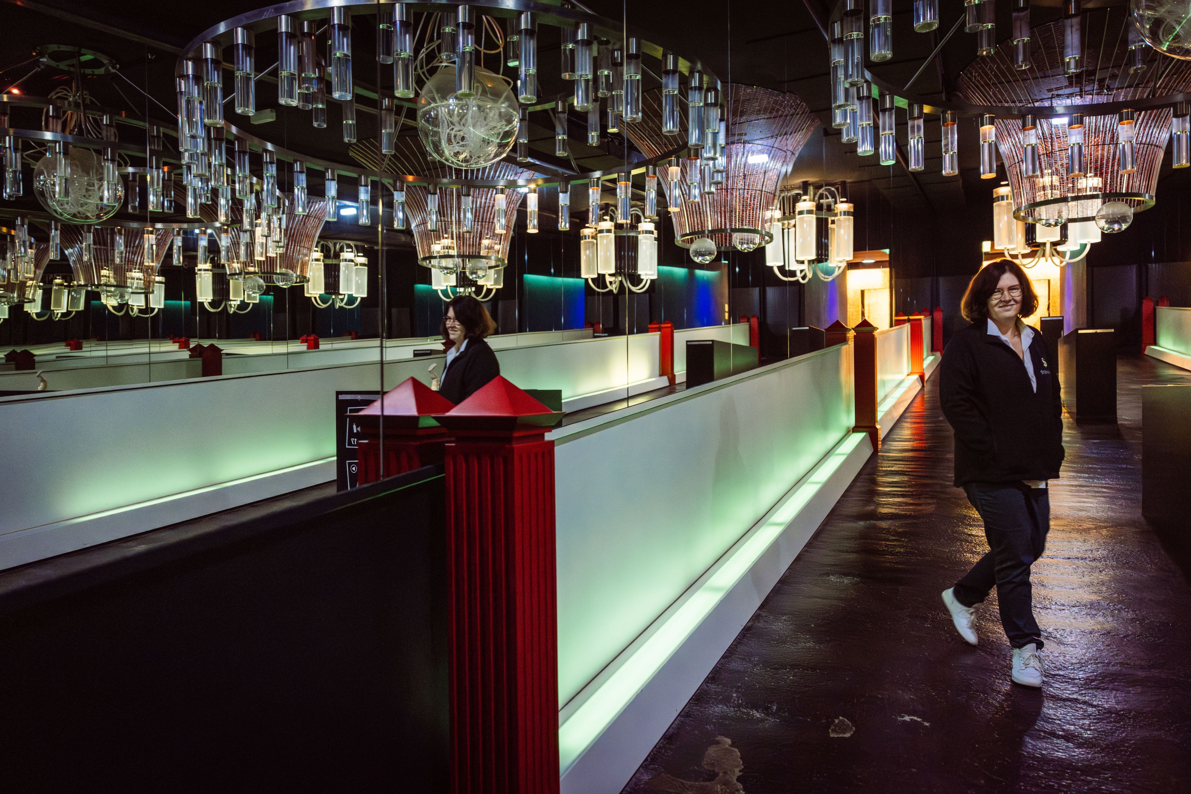 A person in the banquet hall at Steininger Weinwelt during a tour of the wine cellar, surrounded by illuminated glass lamps and mirrored walls.