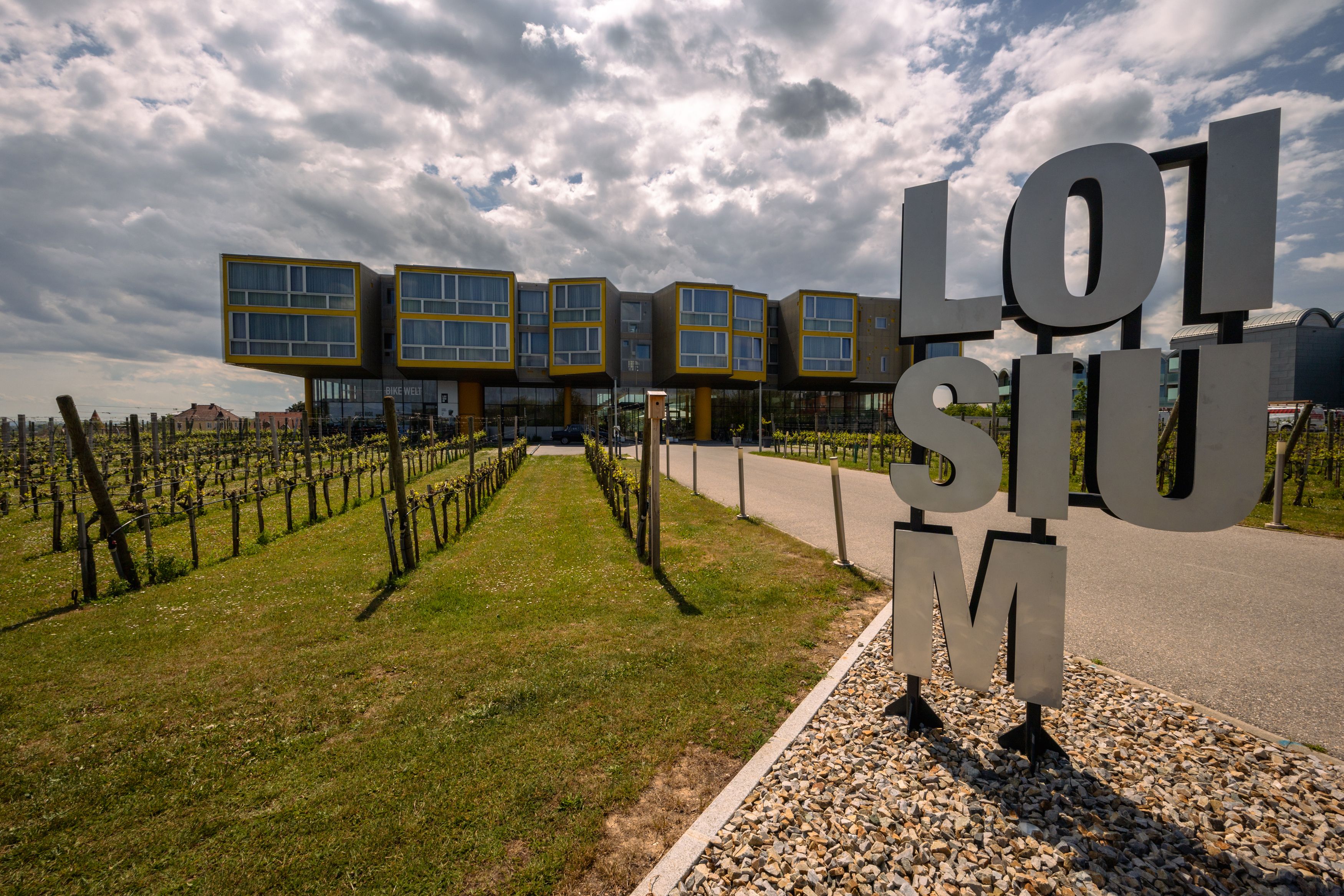 Moderne Architektur des LOISIUM Langenlois mit Weinreben im Vordergrund und bewölktem Himmel.
