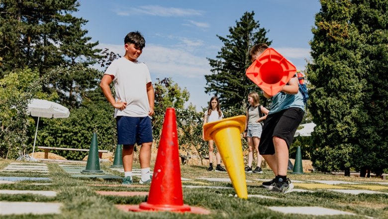 Kinder spielen im Freien mit großen bunten Kegeln auf einem Rasenfeld.