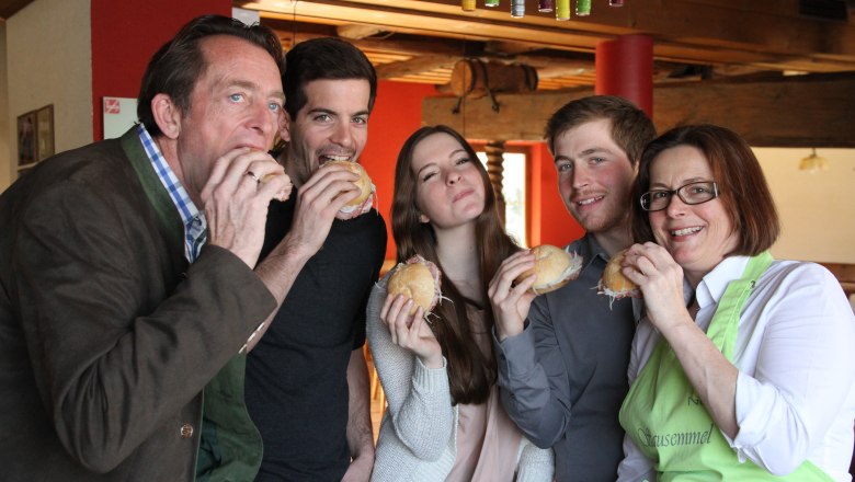 Fünf Personen essen gemeinsam belegte Brötchen in einem gemütlichen Raum.