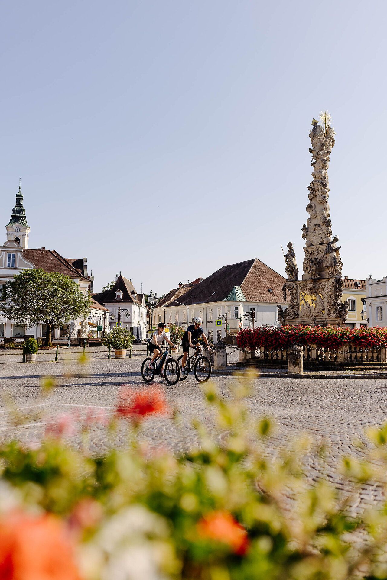 Zwei Radfahrer auf ihren Rädern fahren über den Hauptplatz von Langenlois.