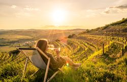 Eine Frau in einem Liegestuhl. Im Hintergrund die Weinberge.