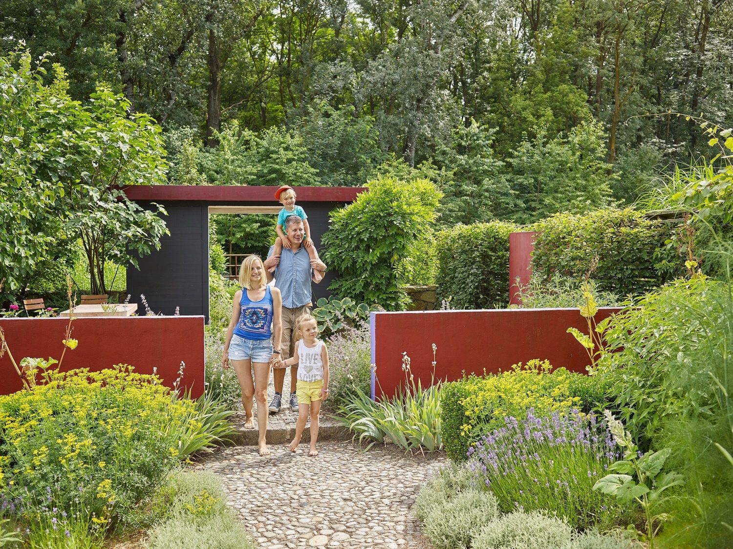 Familie spaziert durch einen Garten mit bunten Blumen und grünen Büschen.