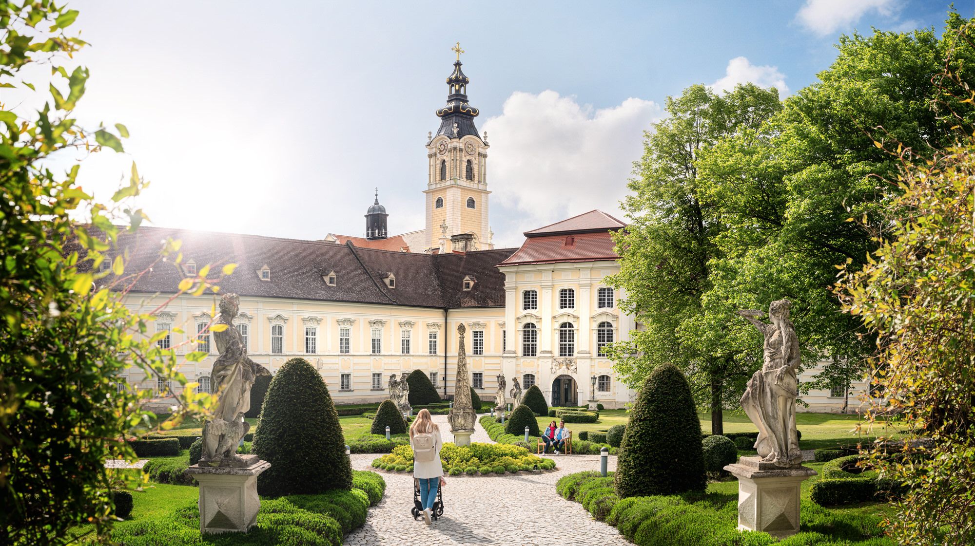Barockes Stift mit Garten und Statuen im Vordergrund.