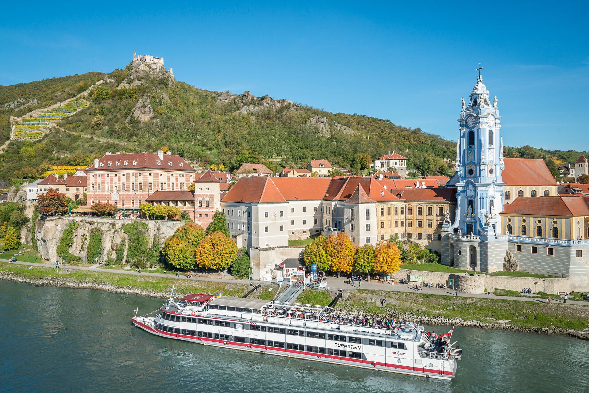 Die malerische Kulisse von Dürnstein, umgeben von sanften Hügeln und der majestätischen Donau, lädt zu einem unvergesslichen Aufenthalt ein. Die bunten Herbstfarben der Bäume spiegeln sich im Wasser wider und schaffen eine harmonische Atmosphäre, die zum Entspannen einlädt.