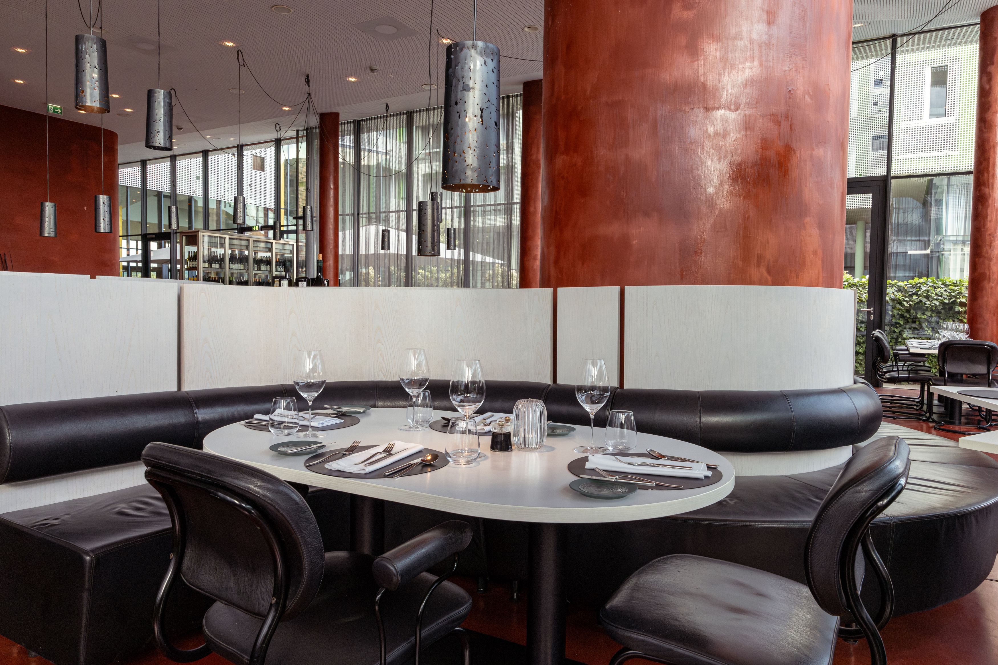 Modernes Restaurant mit gedecktem Tisch, schwarzen Ledersitzen und großen roten Säulen.