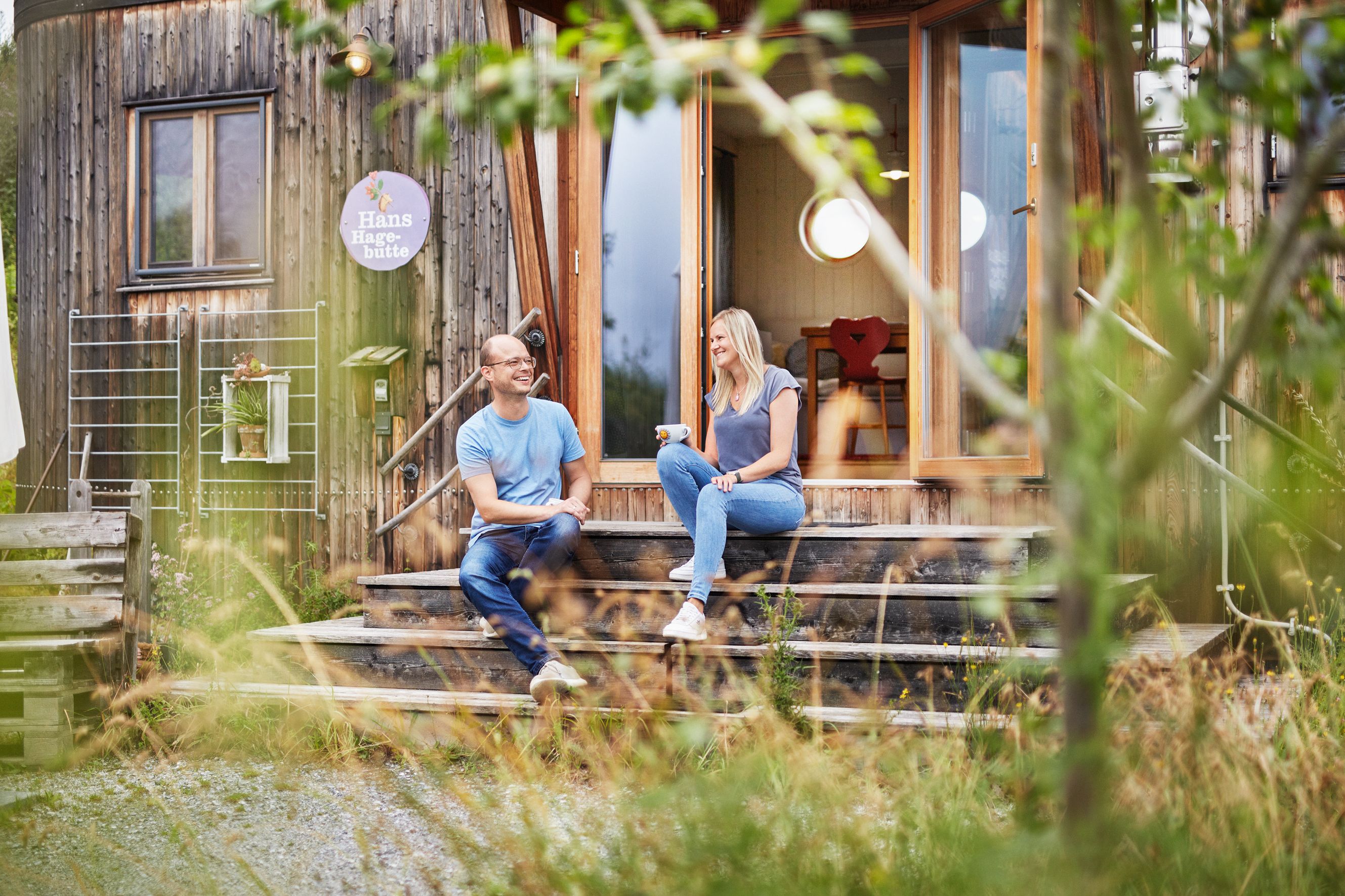 Ein Mann und eine Frau sitzen auf einer Holztreppe vor dem SONNENTOR Landlofts und unterhalten sich.