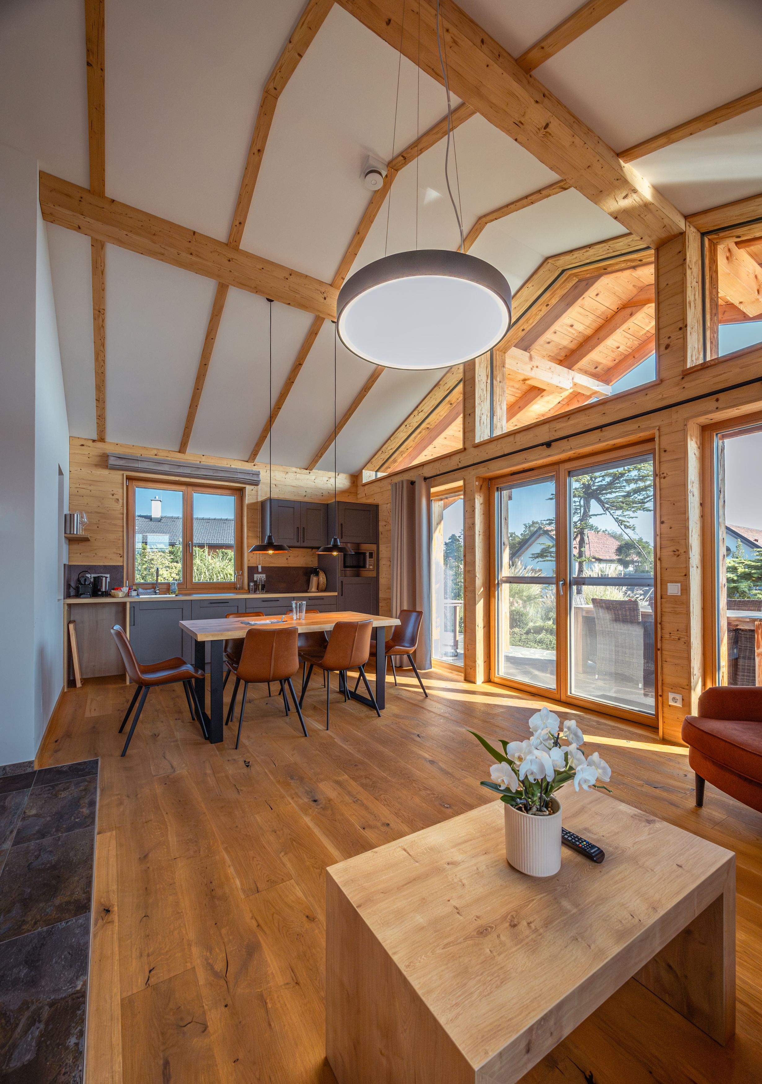 Innenansicht eines modernen Chalets mit Holzbalken, Esstisch und großen Fenstern.