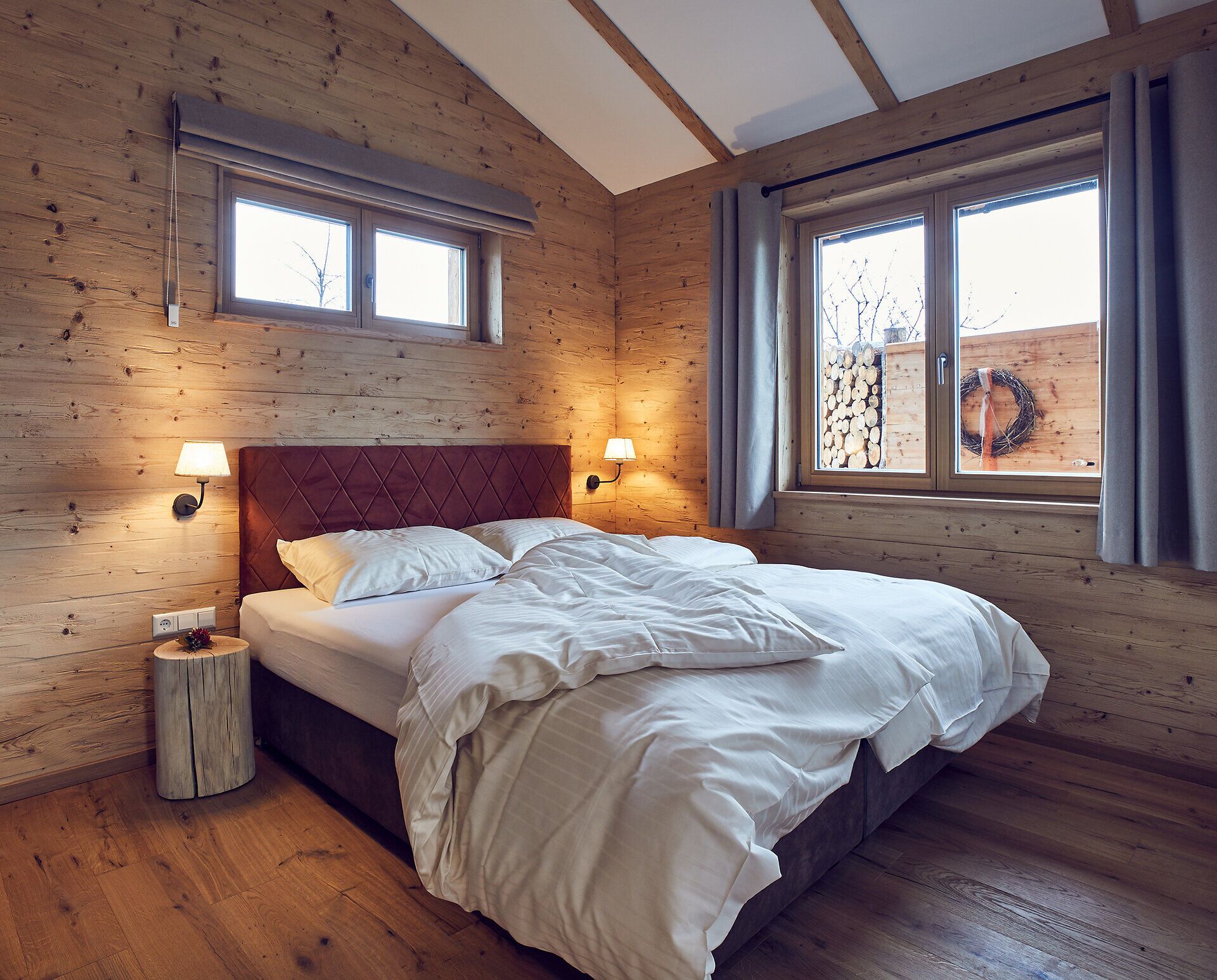 In einem gemütlichen Schlafzimmer mit warmen Holztönen und sanftem Licht lädt die einladende Atmosphäre zum Entspannen ein. Die großen Fenster bieten einen Blick auf die umliegende Natur und schaffen eine harmonische Verbindung zwischen Innen- und Außenbereich. Hier können Gäste die Ruhe und den Komfort genießen, während sie sich auf ihre Erkundungen im Waldviertel vorbereiten.