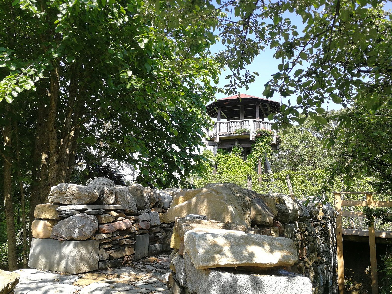 Aussichtsturm der Gartenschule Langenlois umgeben von Bäumen und einer Steinmauer.