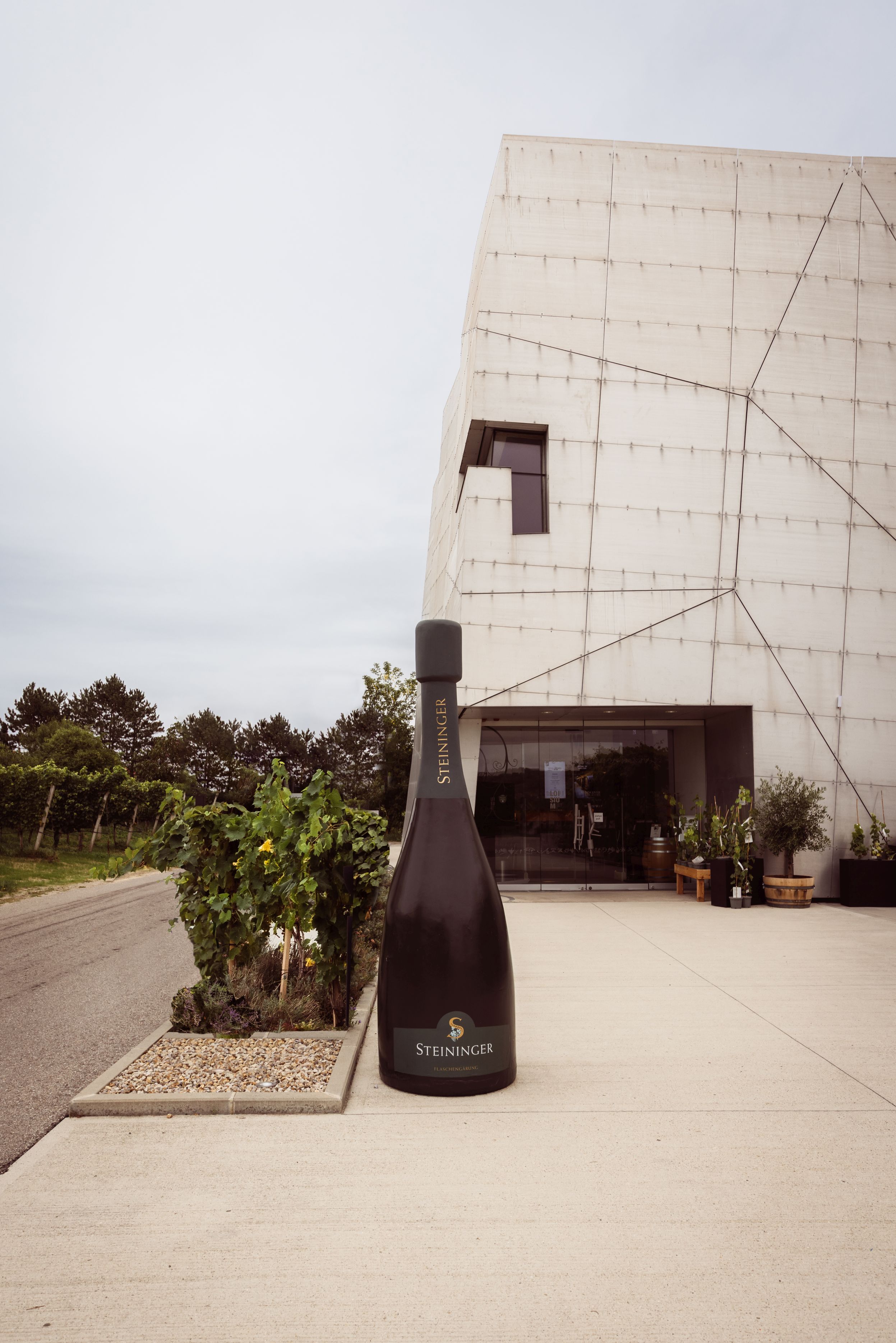 Exterior view of Steininger Weinwelt, featuring a modern facade and an oversized bottle sculpture in front of the entrance.