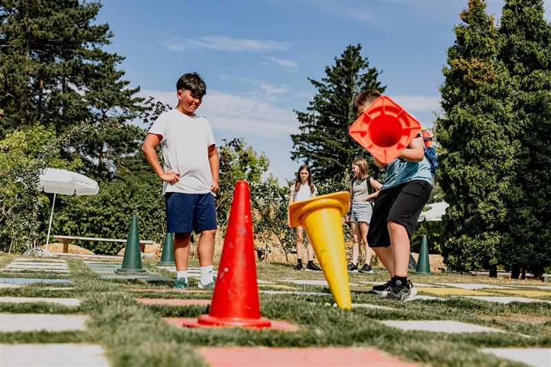 Kinder spielen im Freien mit großen bunten Kegeln auf einem Rasenfeld.