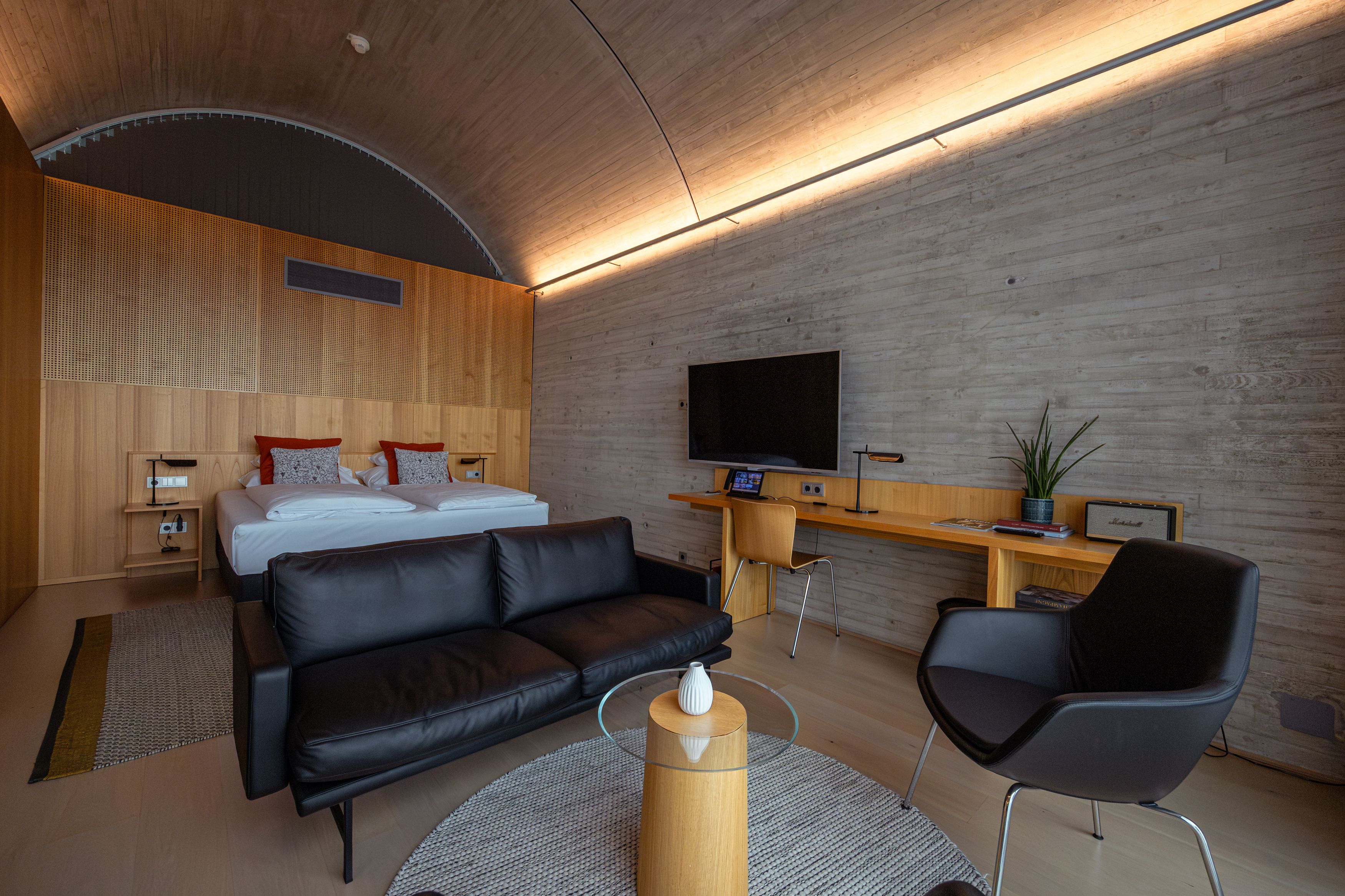 Modernes Hotelzimmer mit Doppelbett, Ledersofa, Schreibtisch und Fernseher.