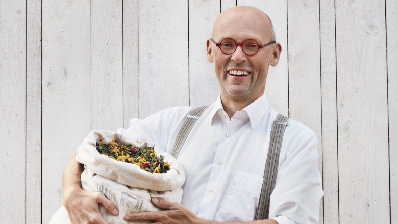 Johannes Gutmann, Gr&uuml;nder von SONNENTOR, h&auml;lt einen Sack voller Kr&auml;uter vor einer Holzwand.