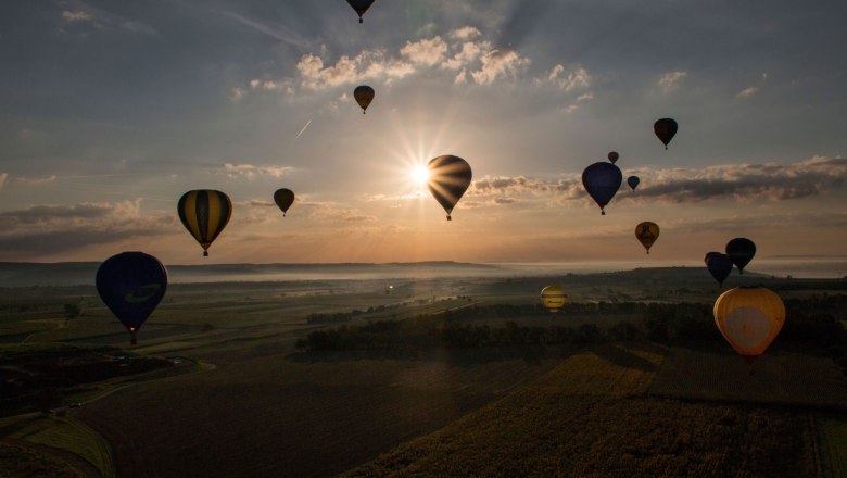 Hei&szlig;luftballons schweben bei Sonnenaufgang &uuml;ber eine Landschaft.