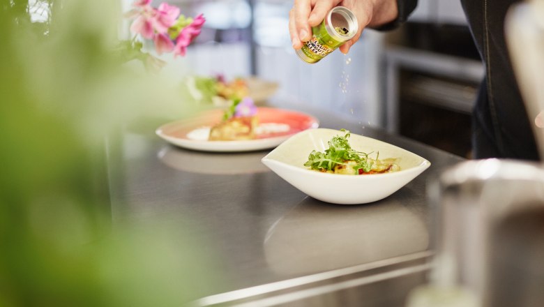Ein Koch w&uuml;rzt ein Gericht in einer Sch&uuml;ssel mit Kr&auml;utern aus einer kleinen Dose.