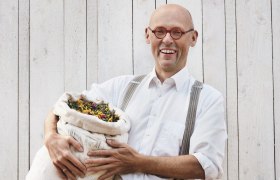 Johannes Gutmann, Gr&uuml;nder von SONNENTOR, h&auml;lt einen Sack voller Kr&auml;uter vor einer Holzwand.