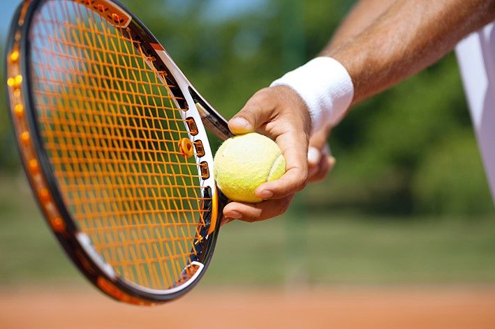 Nahaufnahme eines Tennisspielers, der einen Ball mit einem Schläger auf einem Sandplatz hält.
