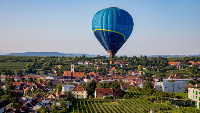 Hei&szlig;luftballon &uuml;ber einer Stadtlandschaft mit Weinbergen und H&auml;usern.