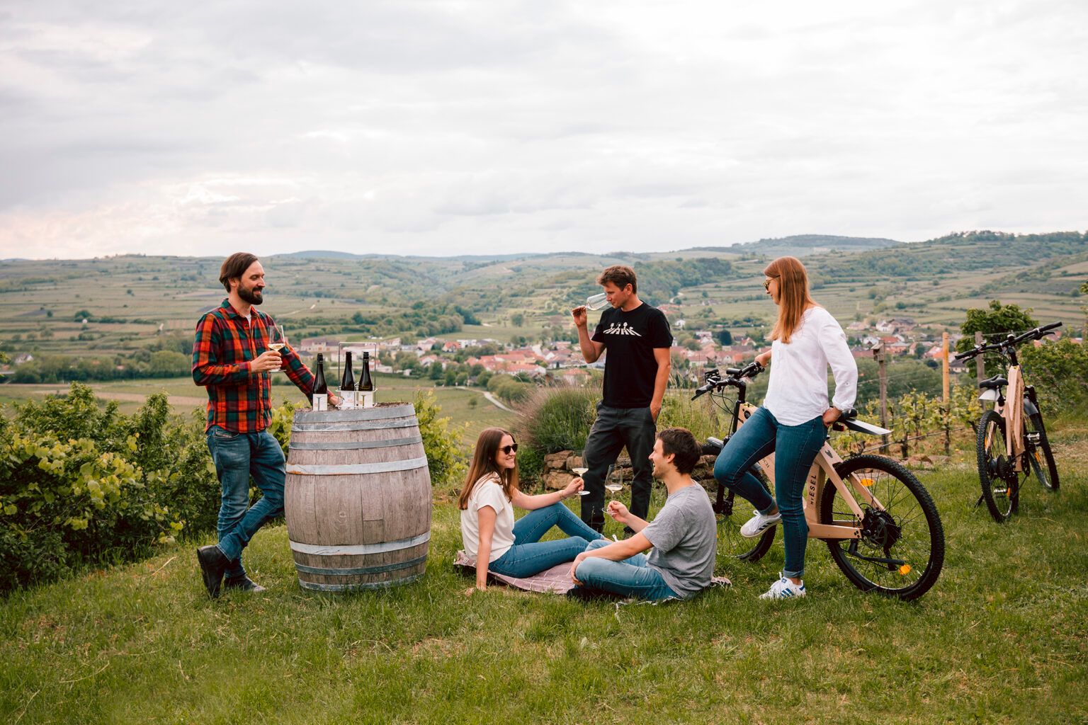 Gruppe von Menschen genießt Wein auf einem Hügel mit Blick auf ein Dorf und Weinberge.