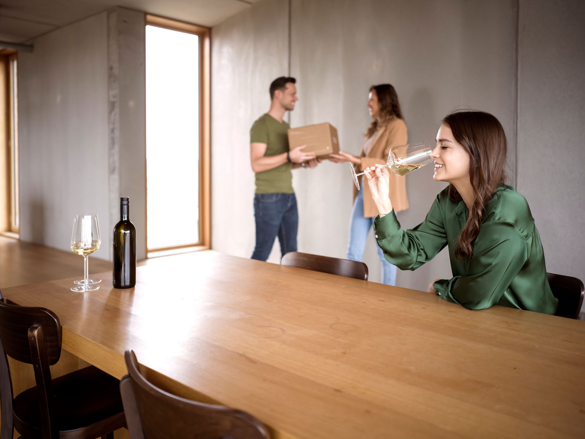 Frau verkostet Wein im Weinglas. Im Hintergrund Frau und Mann.