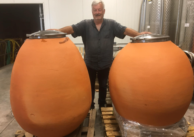 Ein Mann steht zwischen zwei gro&szlig;en, orangefarbenen Tonamphoren in einem Lagerraum.