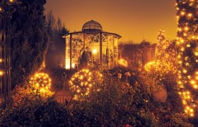 Ein festlich beleuchteter Garten mit einem Pavillon und vielen Lichtern in der D&auml;mmerung.