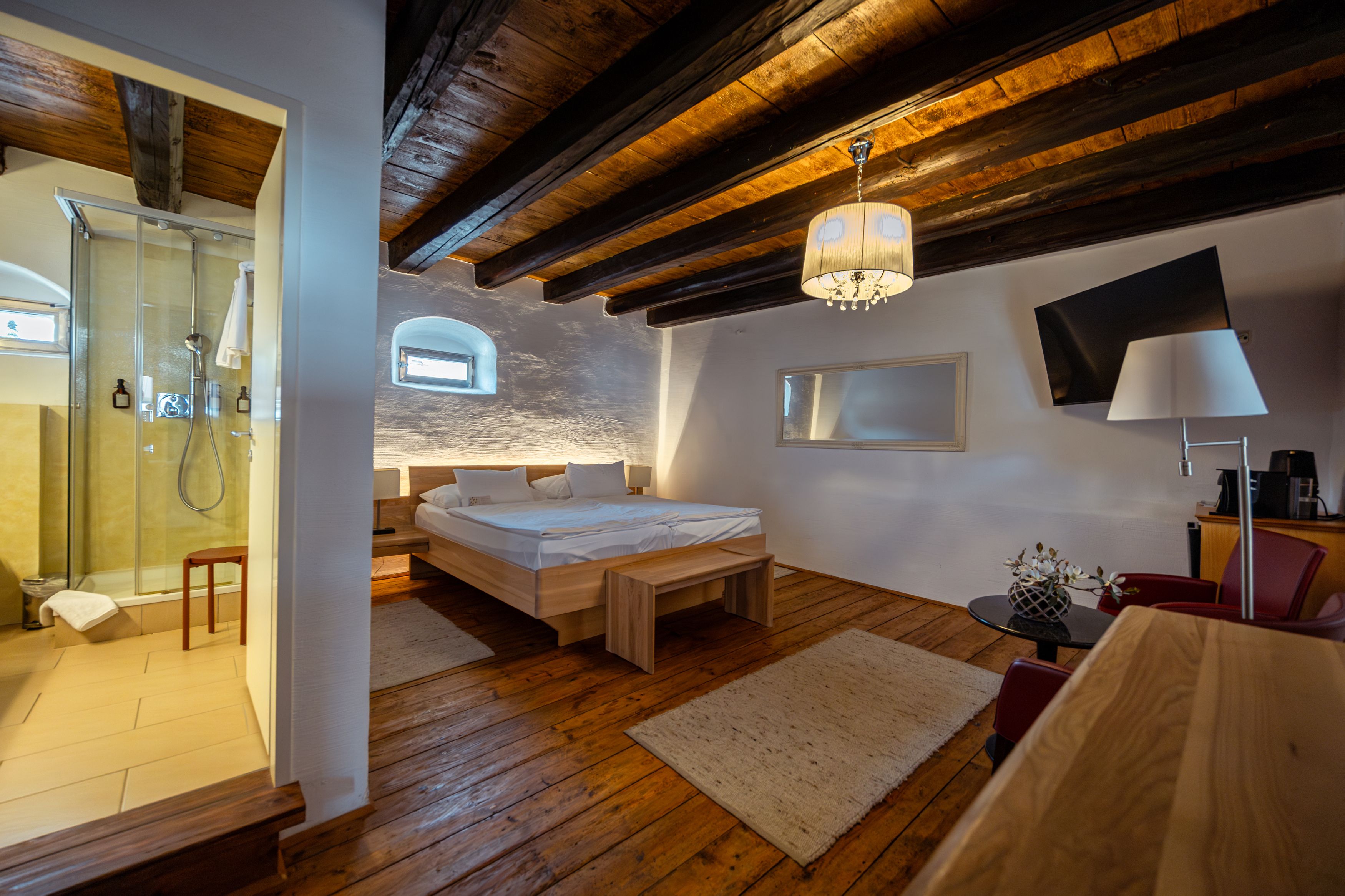 Gemütliches Zimmer mit Holzboden, Doppelbett, Dusche und moderner Einrichtung.