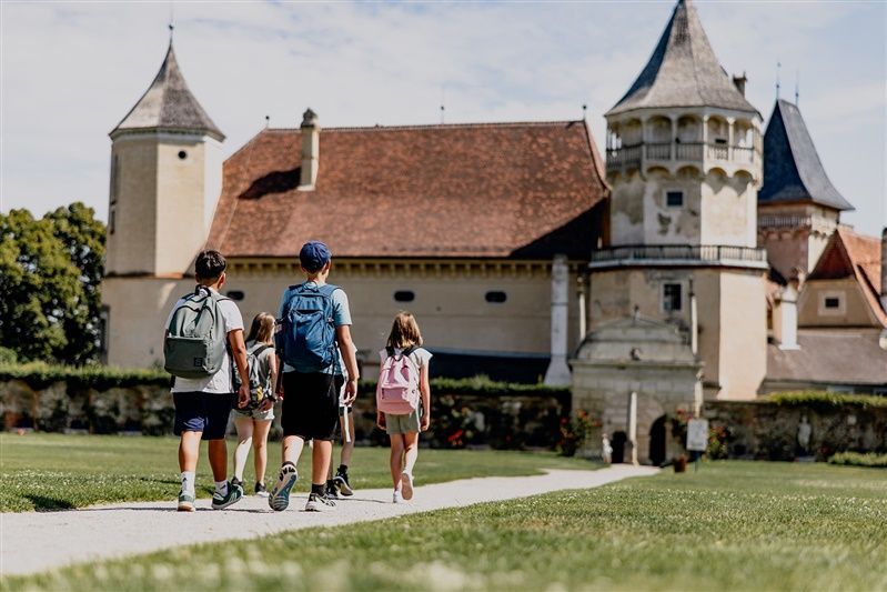 Kinder mit Rucksäcken gehen auf ein Schloss zu.