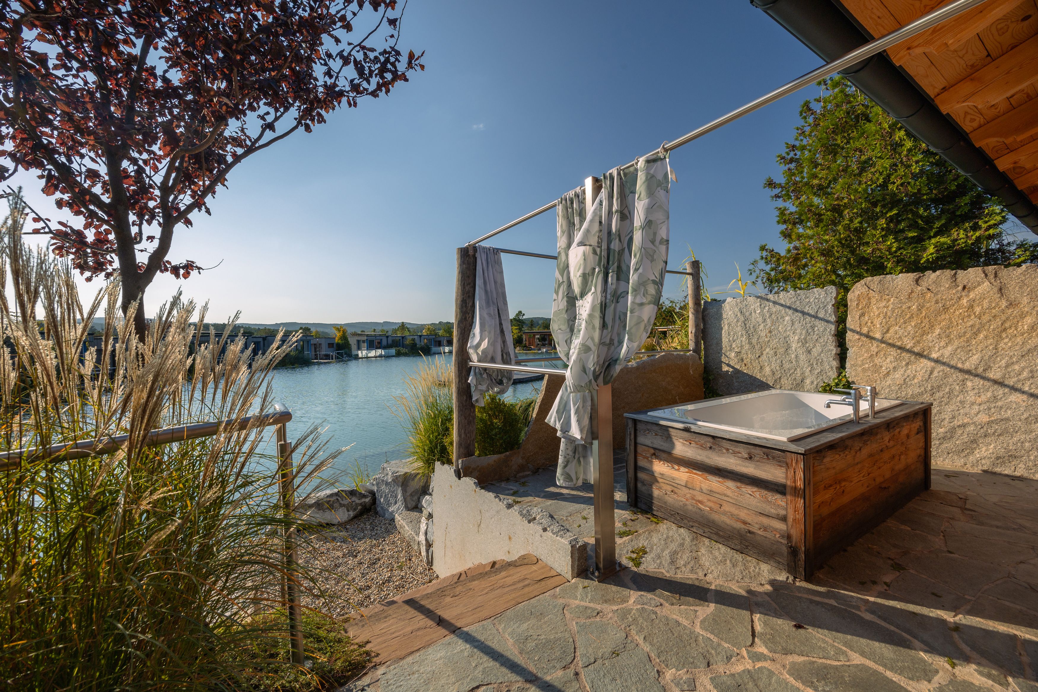 Außenbereich mit Badewanne, Blick auf einen See und Chalets im Hintergrund.