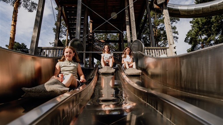 Drei Kinder rutschen auf einer Metallrutsche in einem Park.