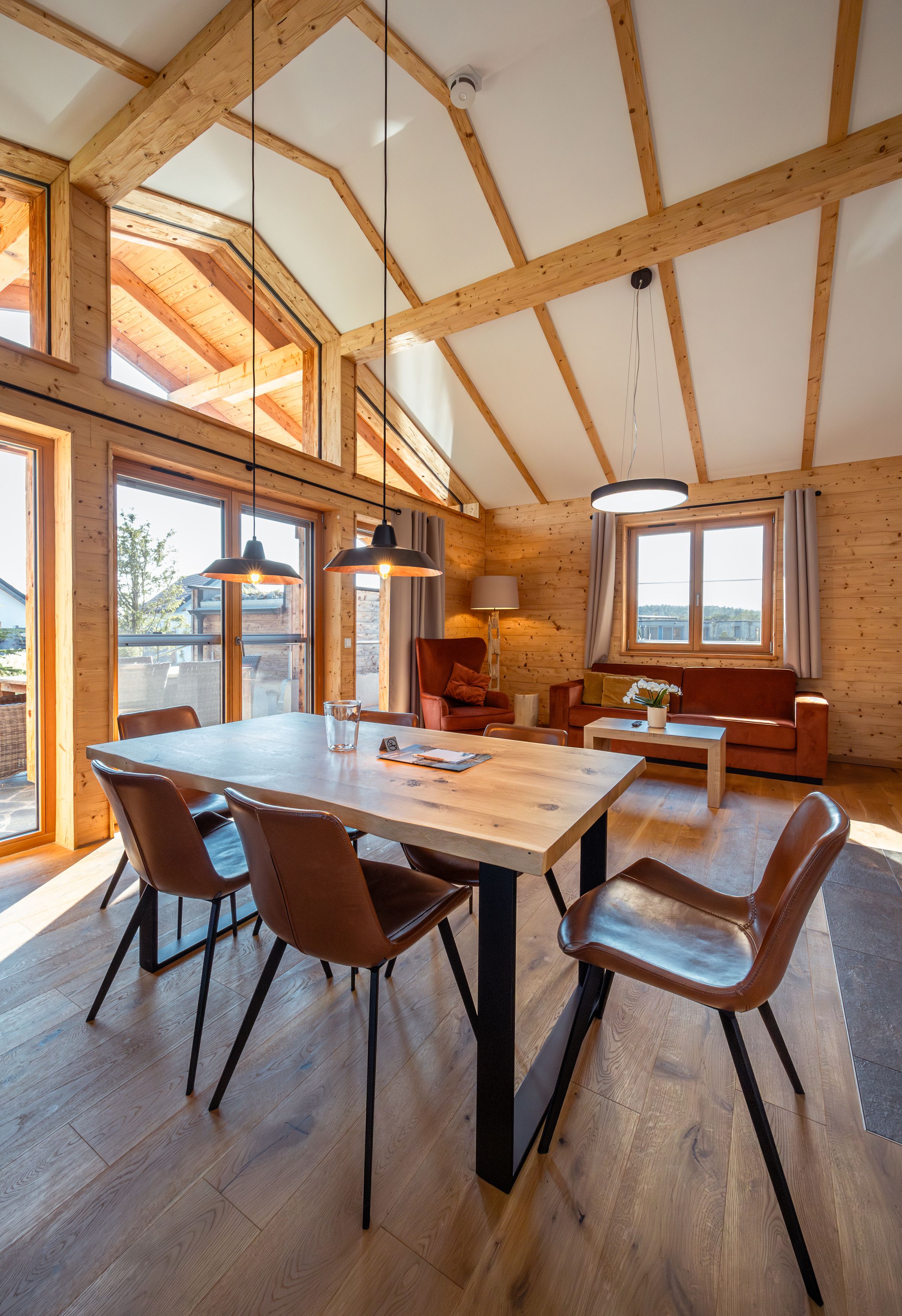 Innenansicht eines modernen Chalets mit Holzwänden, Esstisch und Stühlen, großen Fenstern und gemütlicher Sitzecke.