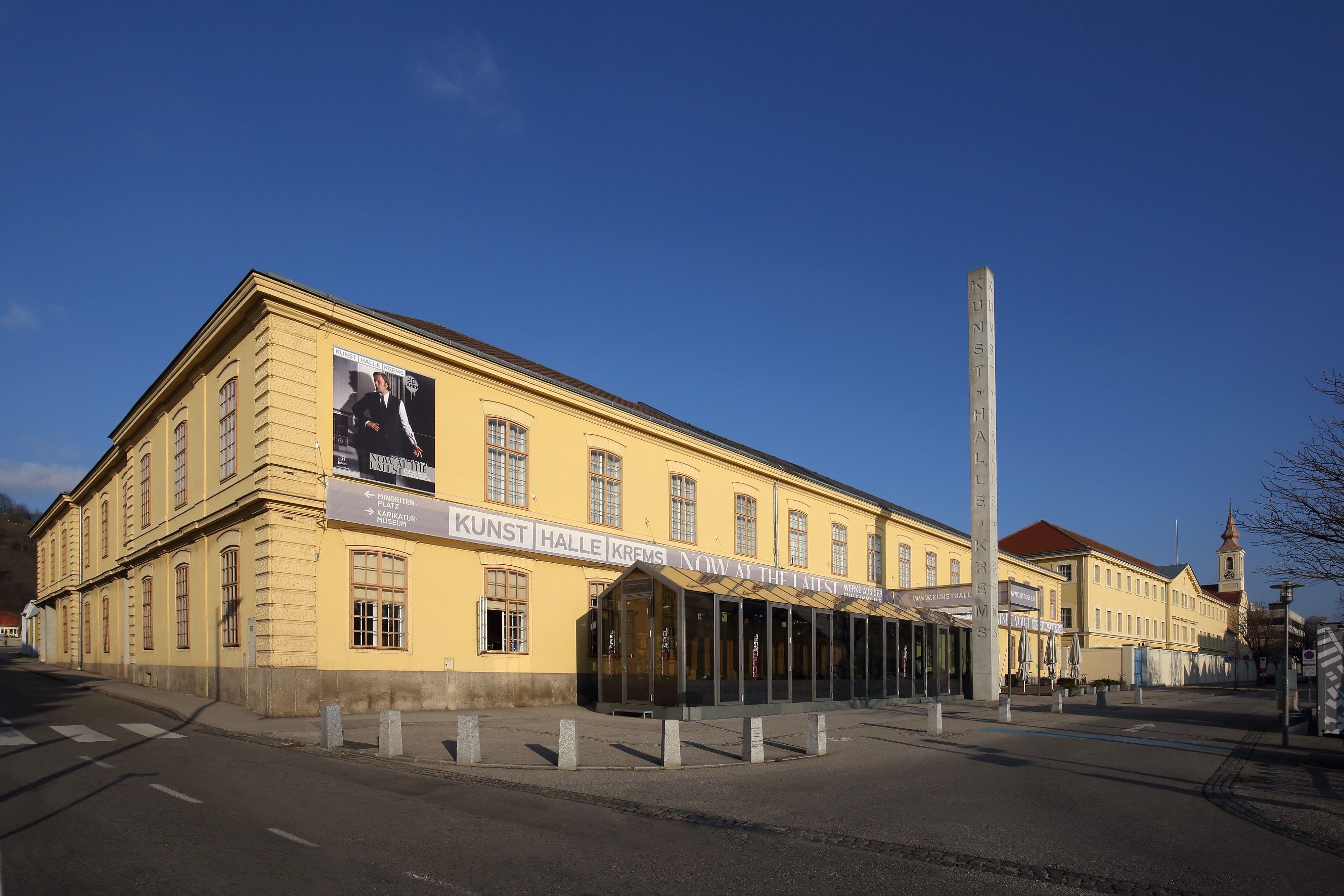 Außenansicht der Kunsthalle Krems, ein gelbes Gebäude mit großen Fenstern und einem Plakat an der Fassade.