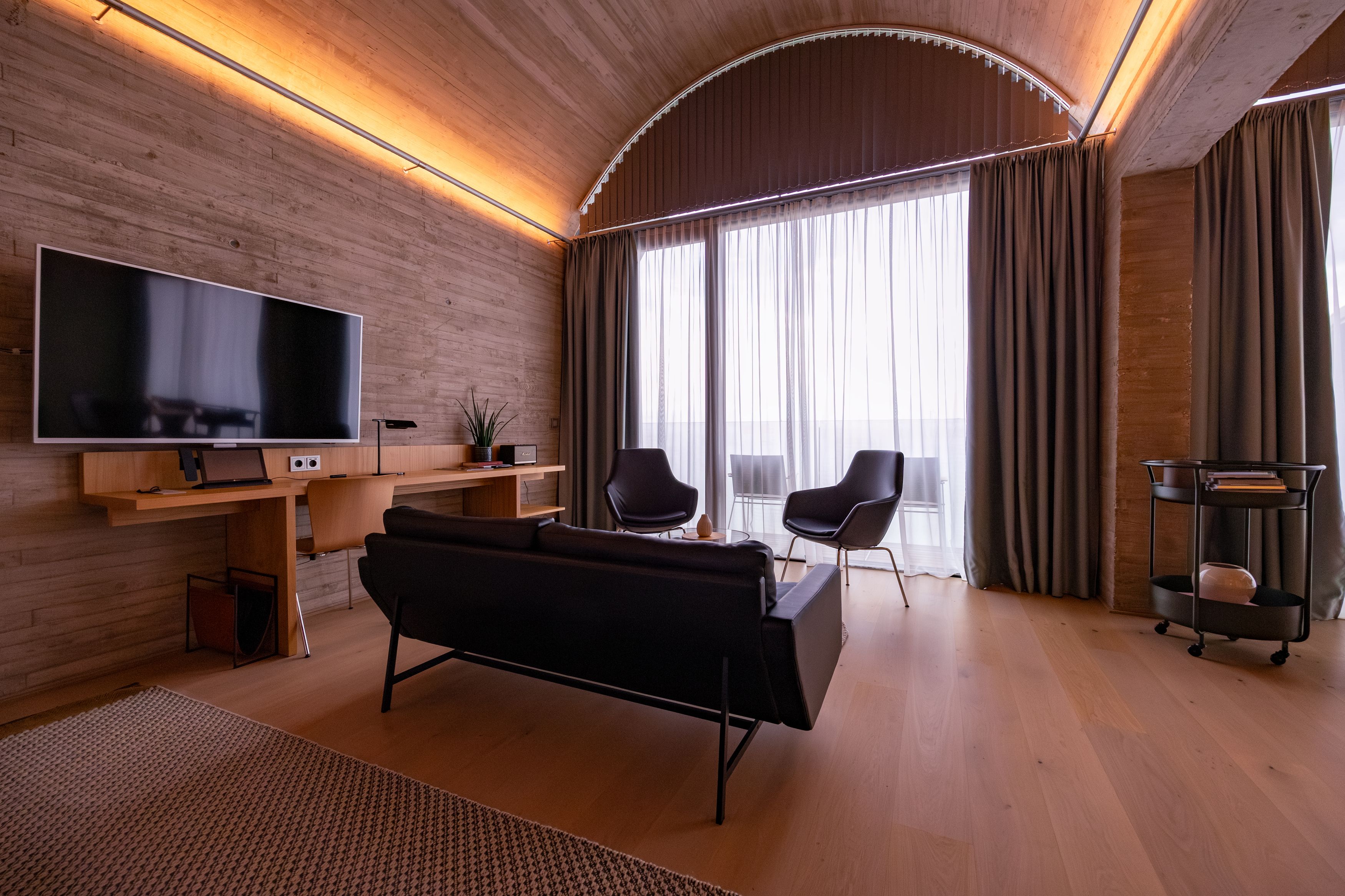 Modernes Wohnzimmer mit Holzdecke, Sofa, Sessel und großem Fenster.