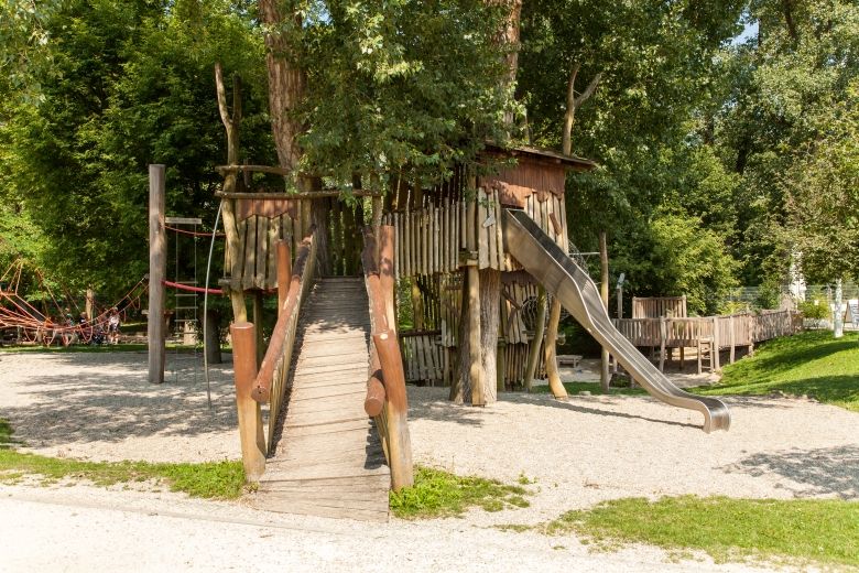 Abenteuer- und Naturspielplatz mit Holzbrücke und Rutsche.