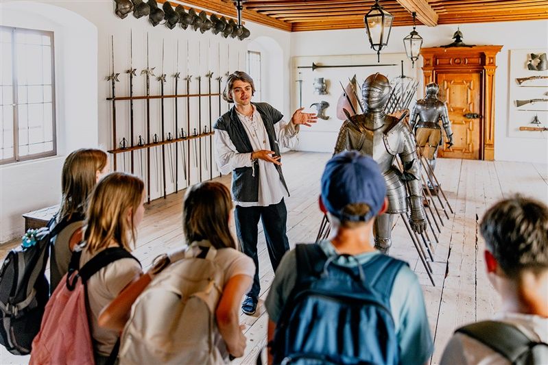 Ein Führer erklärt einer Gruppe von Besuchern eine Rüstung in einem Raum voller mittelalterlicher Waffen im Schloss Rosenburg.